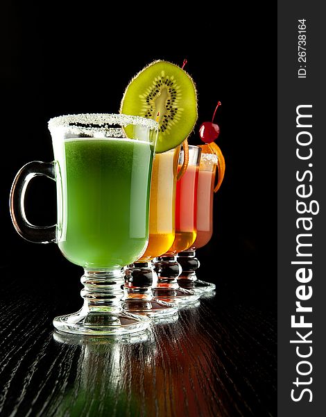 Group of four wine glasses with colored alcoholic cocktails, decorated with fruit and sugar on black bar counter