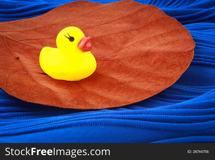 Duck toy on a leaf and on a blue textile (simulation of water)