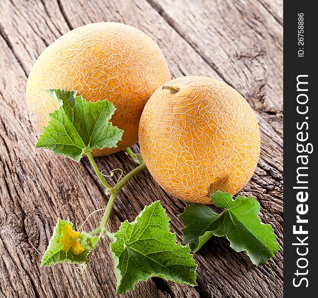 Two melons with the leaves on the old wooden table.