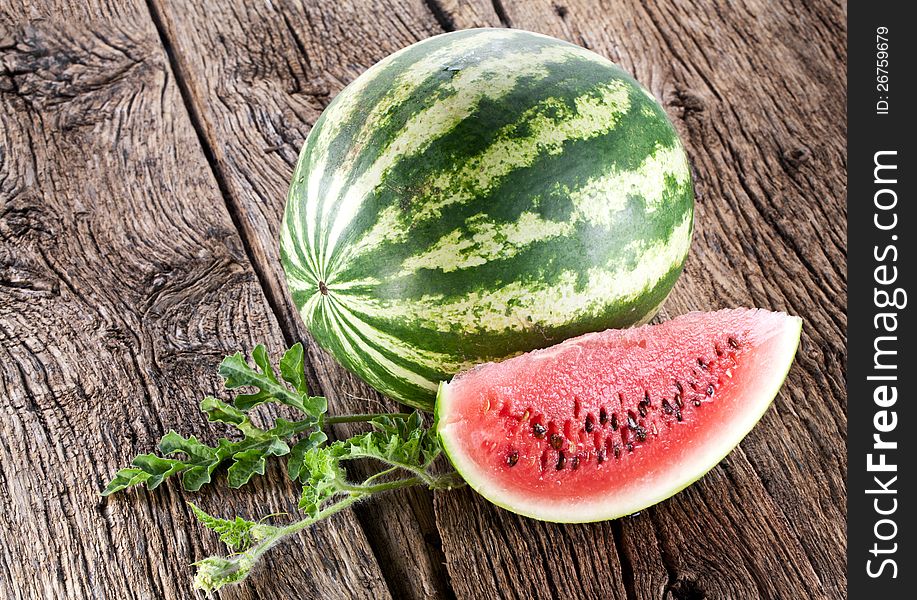 Watermelon with a slice and leaves on a old wooden table.