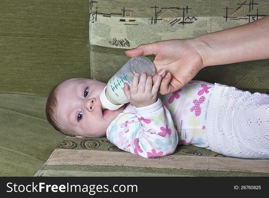 Mom feeds the baby a bottle on the couch. Mom feeds the baby a bottle on the couch