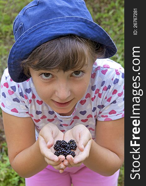 Cute girl showing blackberries in her hands that she has just picked from the garden