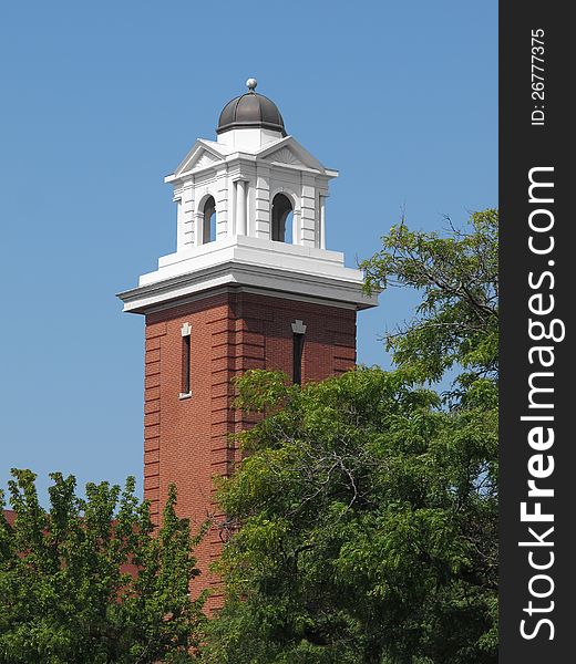 Close-up of a red brick tower with a white top and dome, with trees and a blue sky. Close-up of a red brick tower with a white top and dome, with trees and a blue sky.