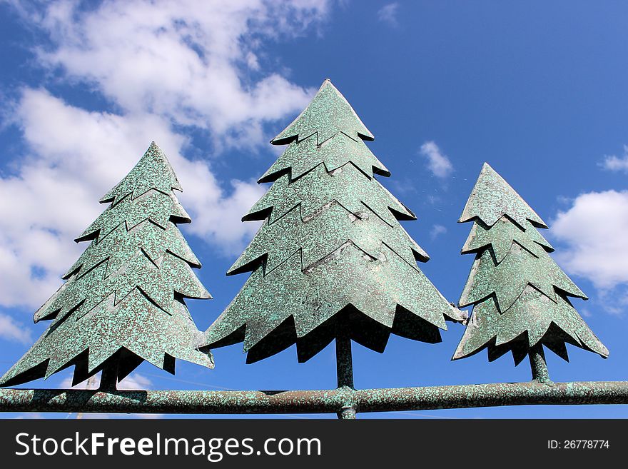 Home decoration of metal pine trees standing against the bright blue sky with puffy cloud cover. Home decoration of metal pine trees standing against the bright blue sky with puffy cloud cover.