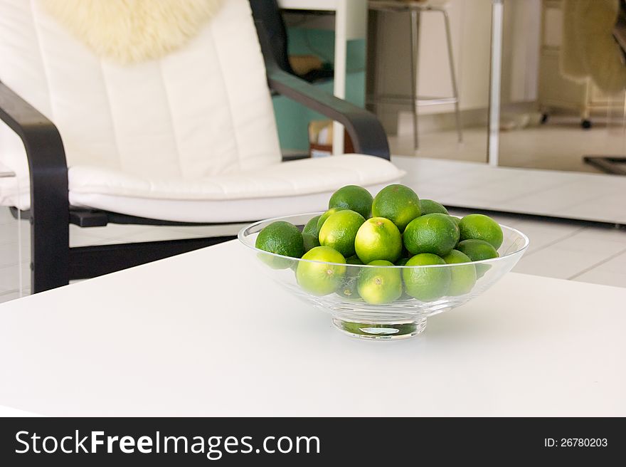 A bowl of fresh limes is placed on a white table inside a home. A bowl of fresh limes is placed on a white table inside a home.