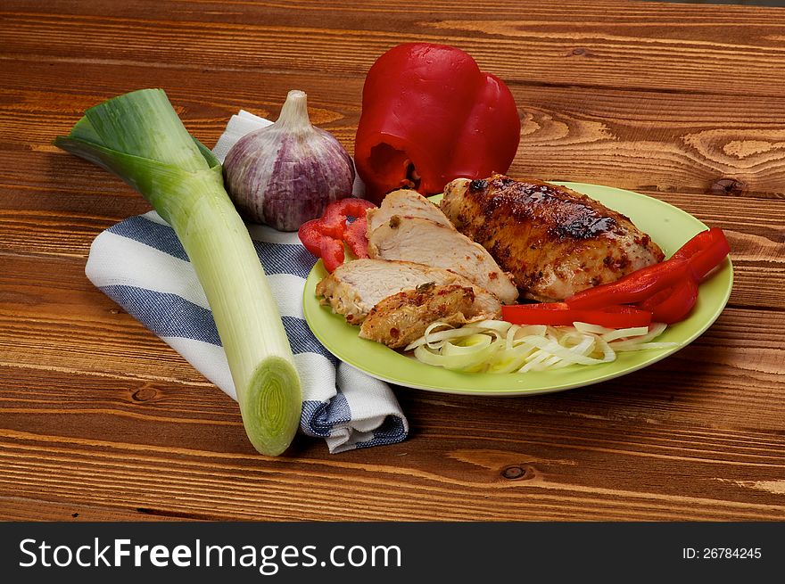 Grilled Chicken Breast with Leek, Garlic and Red Bell Pepper on green plate on wooden background