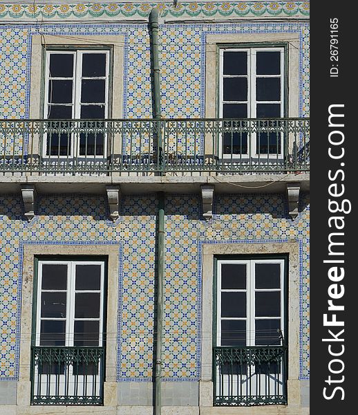 Four windows separated by a drain crossing a balcony are set in a colorful facade of ornamented and glazed tiles on a multistory house in Lisbon, Portugal. Four windows separated by a drain crossing a balcony are set in a colorful facade of ornamented and glazed tiles on a multistory house in Lisbon, Portugal