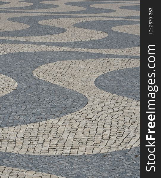 Small cobblestones in dark and light gray form an organic pattern with curved parallel lines on a pavement in Lisbon, Portugal. Small cobblestones in dark and light gray form an organic pattern with curved parallel lines on a pavement in Lisbon, Portugal