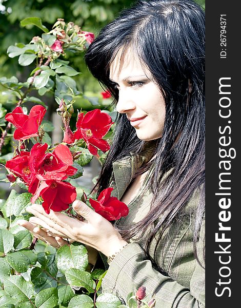 Beautiful brunette near red roses with buds with drops after a rain