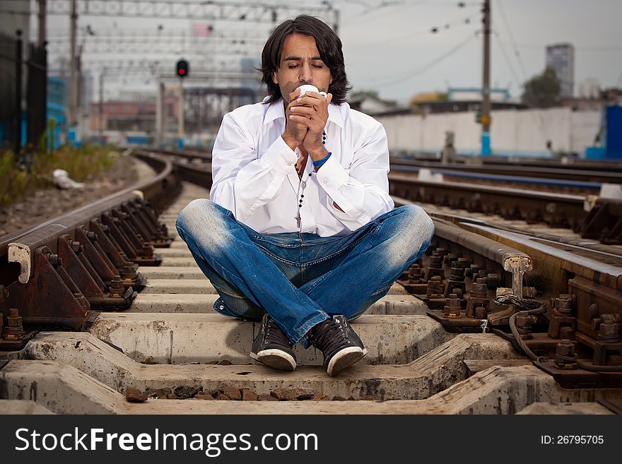 Man is sitting on the rails and drinking coffee. Man is sitting on the rails and drinking coffee