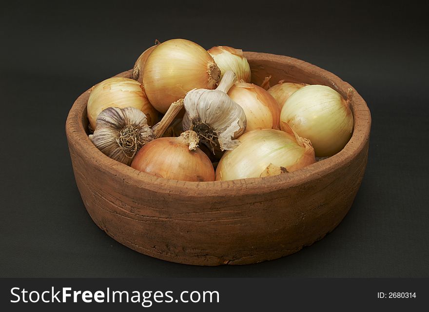Onion and garlic bulbs lying in the ceramic dish