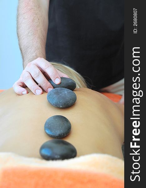 Girl in spa center executing hot stones massage.