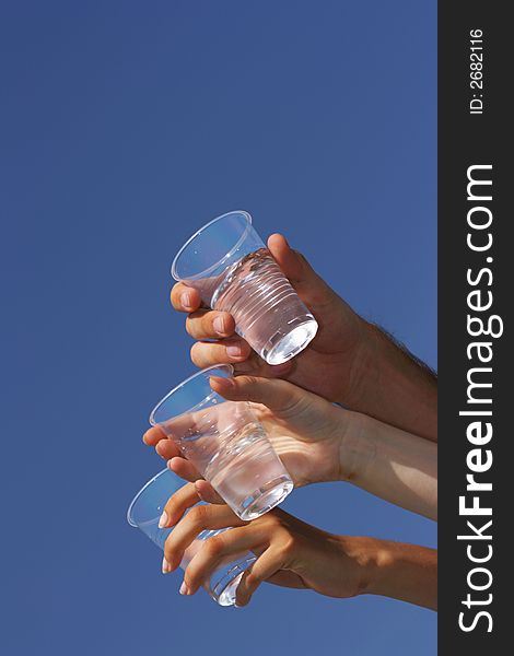 Glasses with transparent beverage in hands against a blue sky. Glasses with transparent beverage in hands against a blue sky