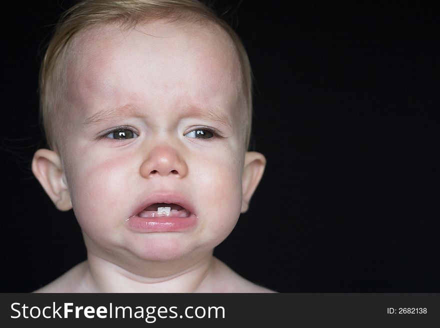 Image of crying toddler sitting in front of a black background