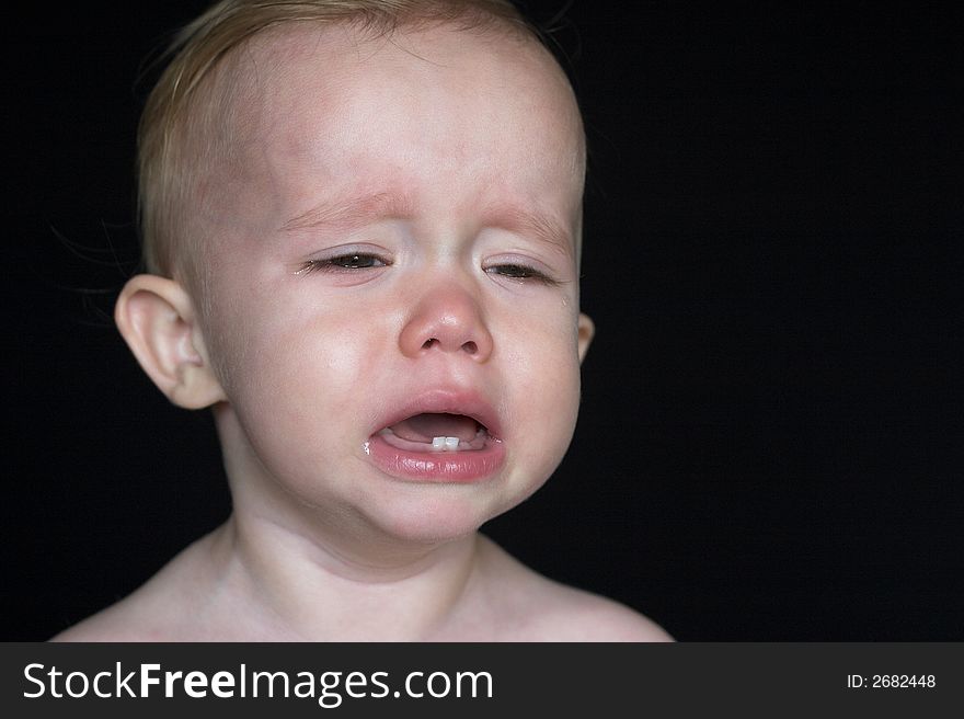 Image of crying toddler sitting in front of a black background