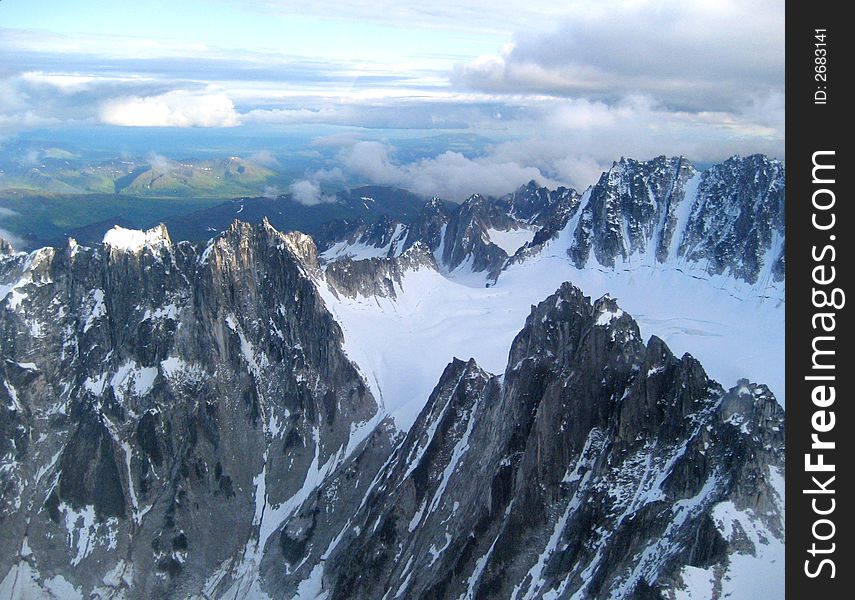 Flying over Alaska, snowy mountains of rock, green ranges in the background. Flying over Alaska, snowy mountains of rock, green ranges in the background