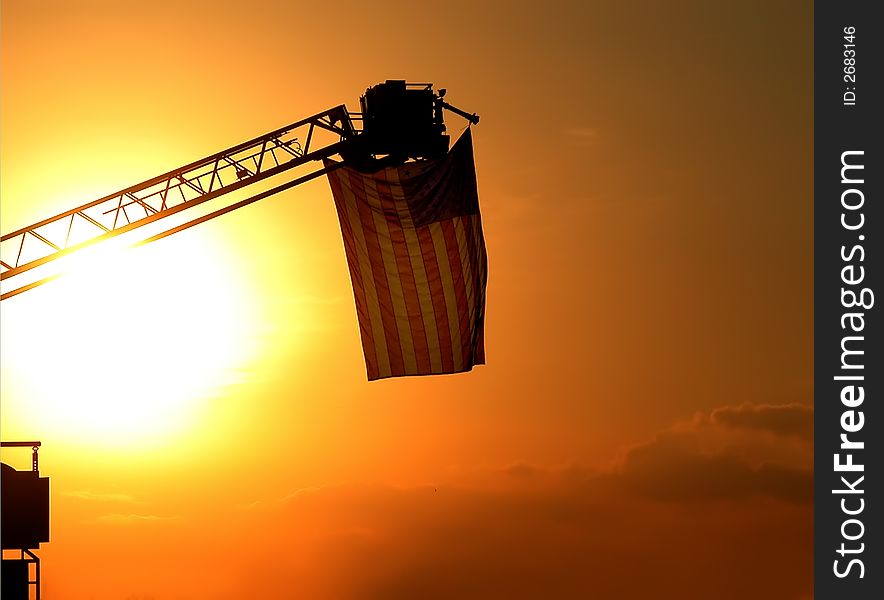 An American flag hanging in the sunset on the top of a fire truck ladder. An American flag hanging in the sunset on the top of a fire truck ladder.
