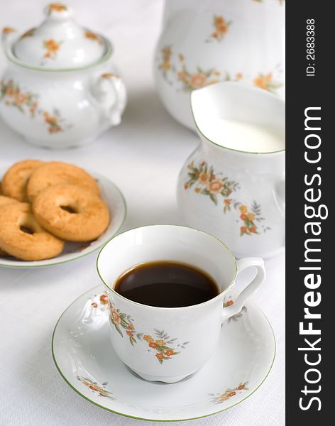 Coffee (or tea) set on the table - cup of coffee on the front (focus on it) cookies, milk jug and sugar bowl behind. Coffee (or tea) set on the table - cup of coffee on the front (focus on it) cookies, milk jug and sugar bowl behind.