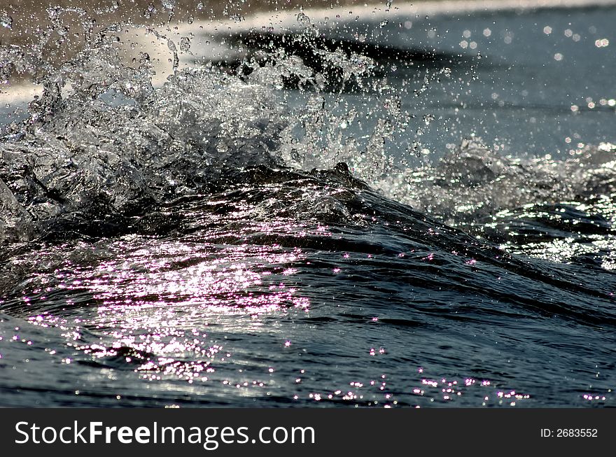 Spray of little sea wave on a beach, back light