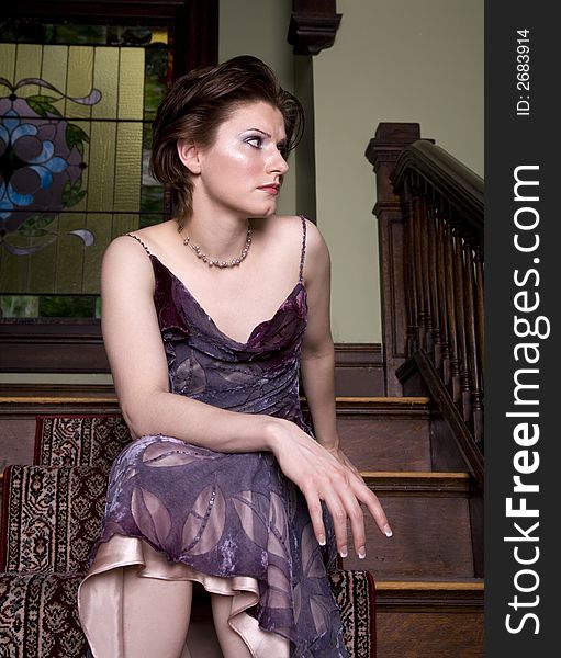 Beautiful young brunette woman wearing a dress sitting on a staircase waiting expectantly. Beautiful young brunette woman wearing a dress sitting on a staircase waiting expectantly.