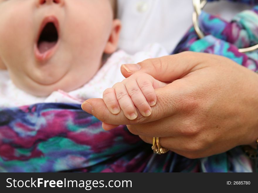 The hands of a mother and child with a baby yawning in the background. The hands of a mother and child with a baby yawning in the background