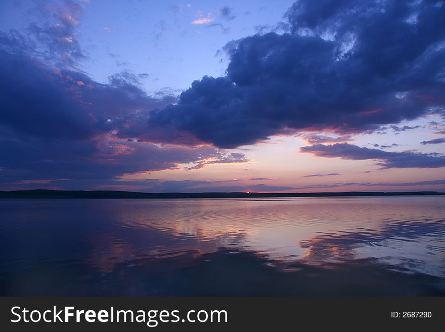 Sunset with the sun and clouds reflected in water. Sunset with the sun and clouds reflected in water.