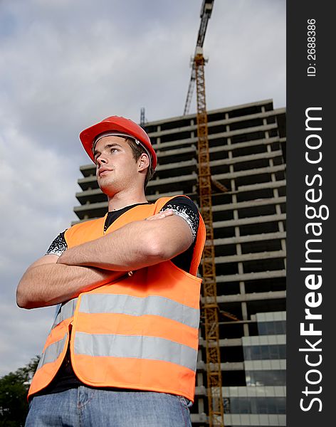 Construction supervisor in safety helmet and reflex vest in front of construction site.