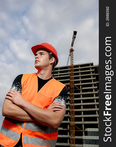 Construction supervisor in safety helmet and reflex vest in front of construction site.