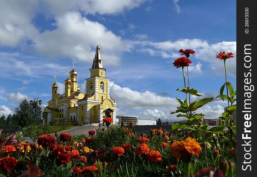 Nadym. The Orthodox temple with flowerses on background blue sky. Nadym. The Orthodox temple with flowerses on background blue sky.