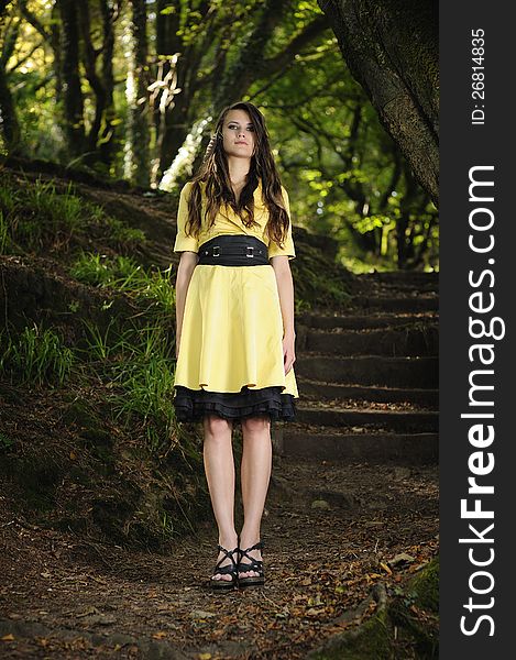A girl standing in a forest with a yellow dress on. A girl standing in a forest with a yellow dress on.