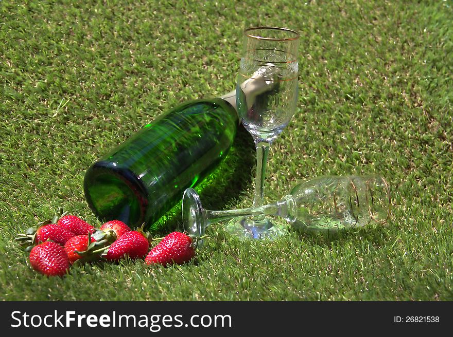 Champagne bottle, glasses and strawberries on the green grass