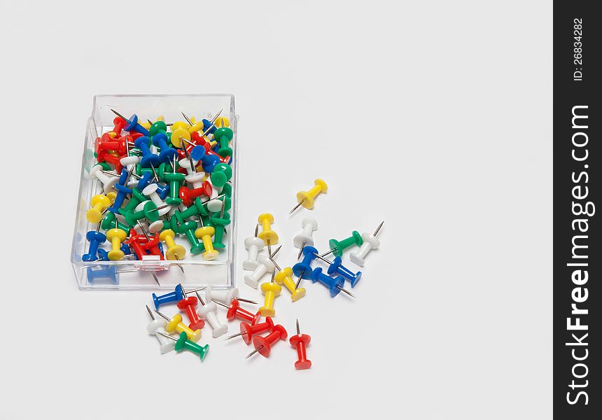 A pile of coloured thumbtacks lying in the box and on white background. A pile of coloured thumbtacks lying in the box and on white background