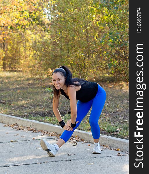 Happy woman exercising in a park bending forwards on her extended leg to stretch her muscles while warming up
