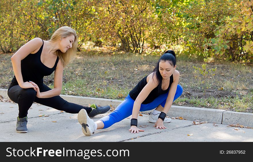 Two attractive young women athletes training outdoors doing stretching exercises while working out in the park