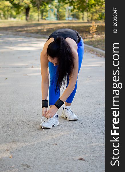 Woman athlete in sportswear bending down and tying her shoelaces on her trainers before starting her exercises in the park. Woman athlete in sportswear bending down and tying her shoelaces on her trainers before starting her exercises in the park
