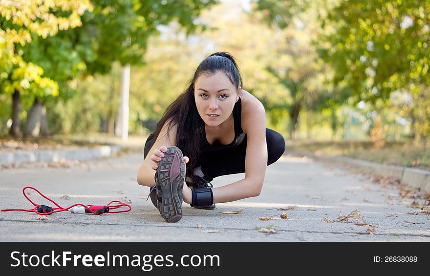 Low angle view of a young attractive woman athlete stretching with her leg extended close to the road surface as she warms up for her workout and training. Low angle view of a young attractive woman athlete stretching with her leg extended close to the road surface as she warms up for her workout and training