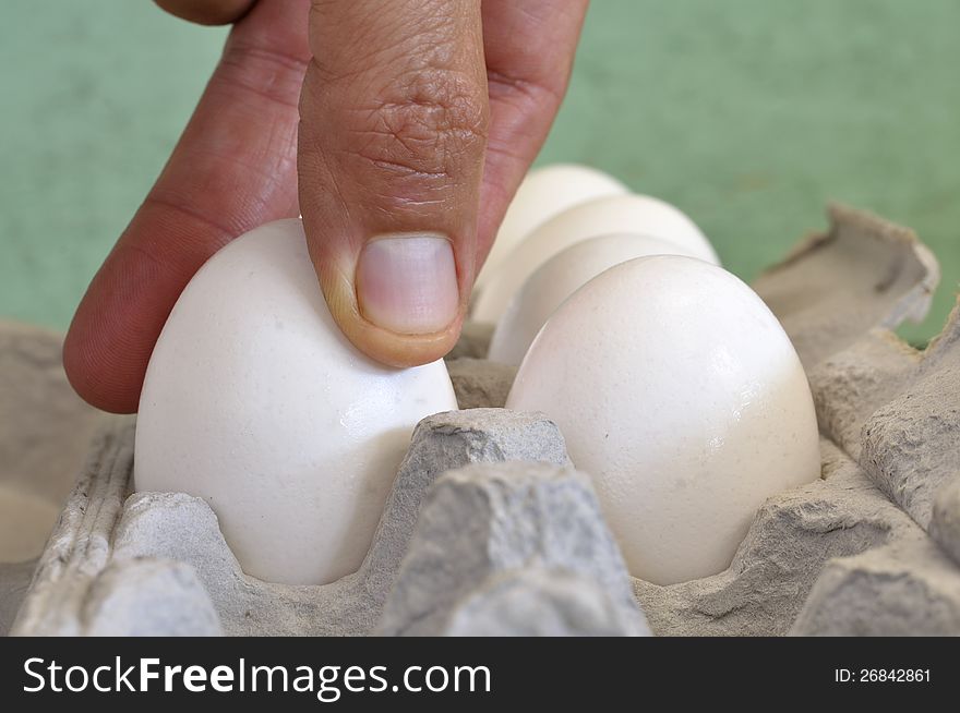 Closeup of fingers of man grabbing an egg from carton. Closeup of fingers of man grabbing an egg from carton