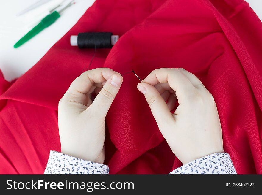 Female hands sews red fabric. A girl holds a needle in her hands. Small business.