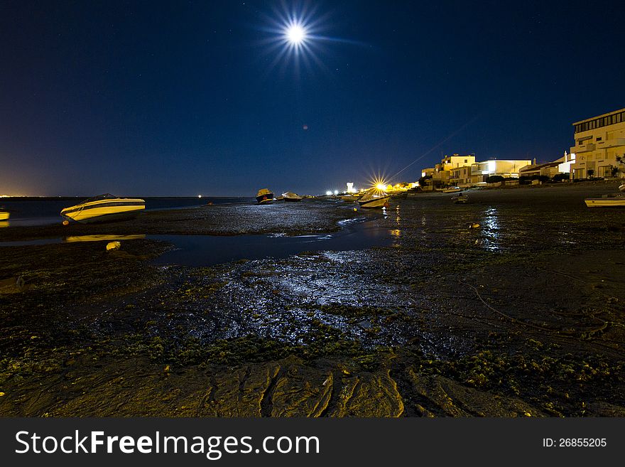 View of a beach in the moonlight with boats anchored in the sand. View of a beach in the moonlight with boats anchored in the sand.