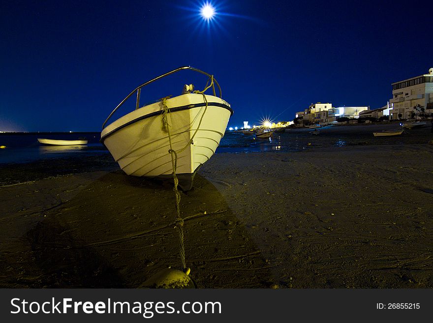 Close view of a white and blue traditional fishing boat anchored on a beach at night.