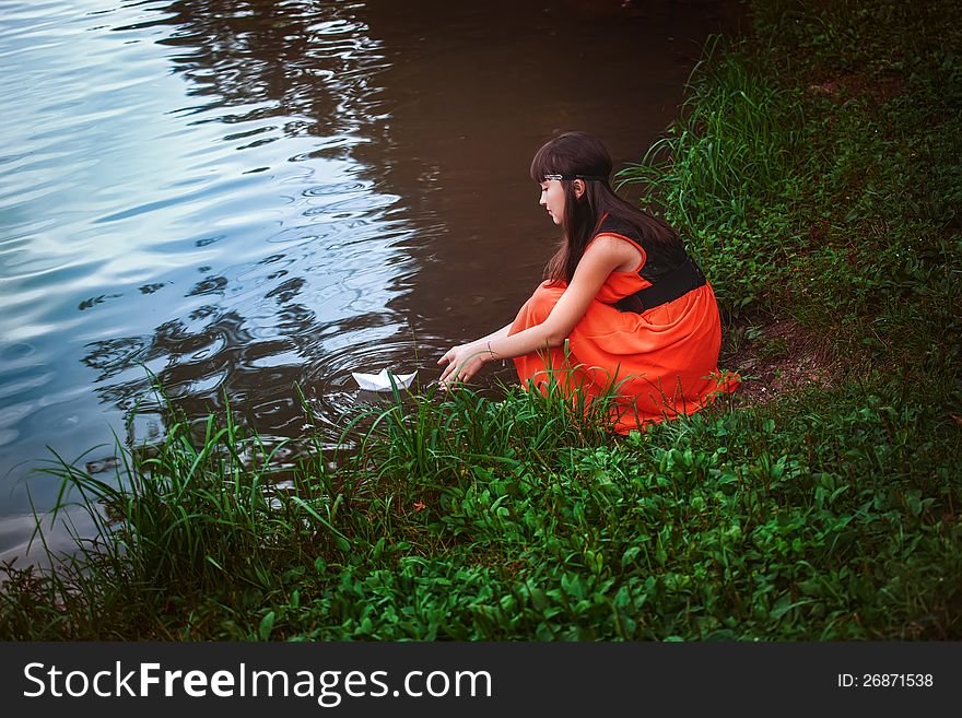 Girl in red dress sitting by a lake. Girl in red dress sitting by a lake