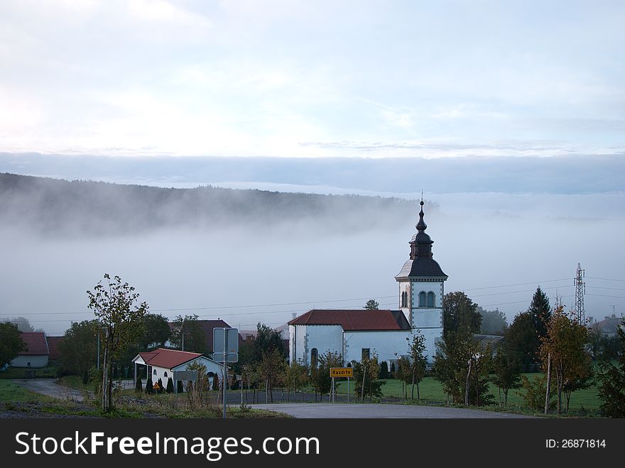 Morning village with church and fog in background.