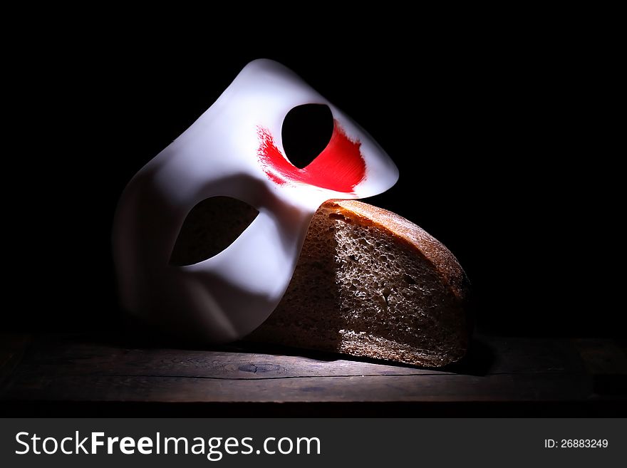 Roman Empire concept. White mask with red spot lying on bread on black background. Roman Empire concept. White mask with red spot lying on bread on black background