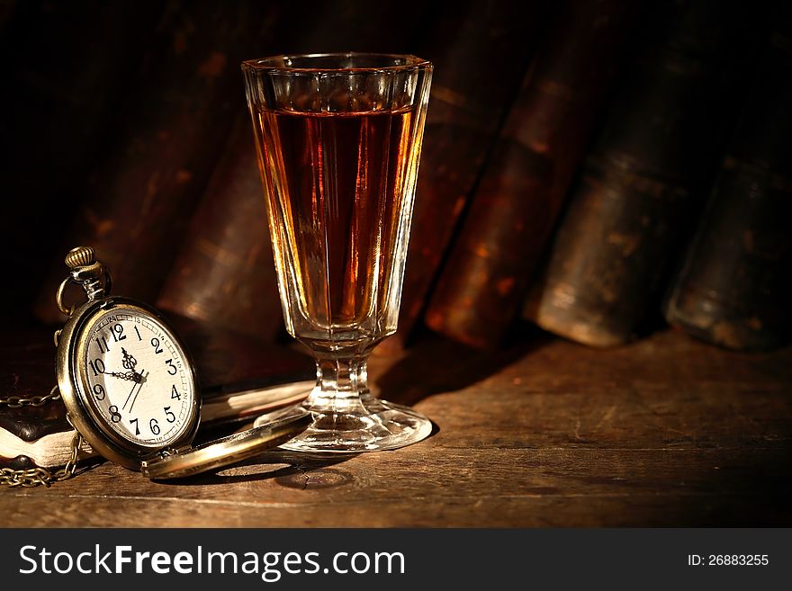 Vintage small wineglass with alcohol near open pocket watch on background with old books. Vintage small wineglass with alcohol near open pocket watch on background with old books