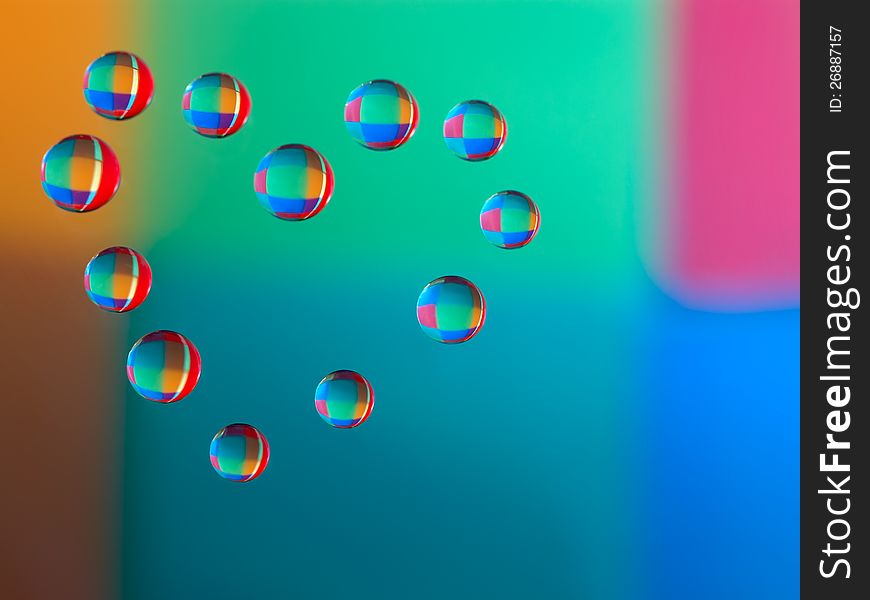 Drops of water on glass in a heart shaped. Colorful background is reflected in the drops. macro. Drops of water on glass in a heart shaped. Colorful background is reflected in the drops. macro