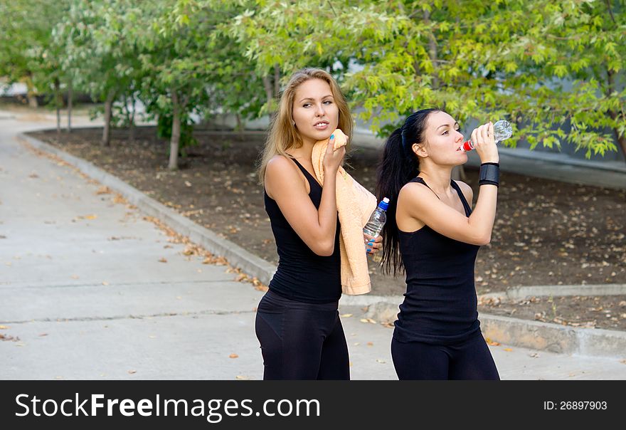 Women athletes taking a break during training having a refreshing drink of bottled water
