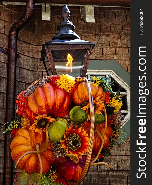 Fall Decoration on rustic lamp with flame and rustic building in back ground.