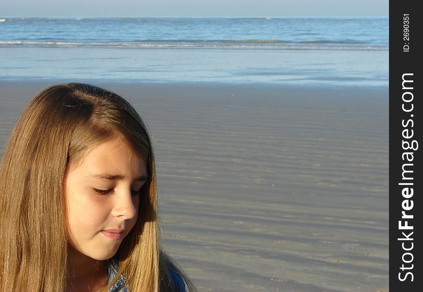 Young girl standing on the beach, looking at the sand. Young girl standing on the beach, looking at the sand