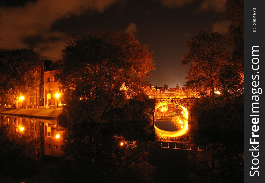 A night view of illuminated (classic) bridge and houses in a European city with a reach and long history. With a canal on the foreground. A night view of illuminated (classic) bridge and houses in a European city with a reach and long history. With a canal on the foreground.