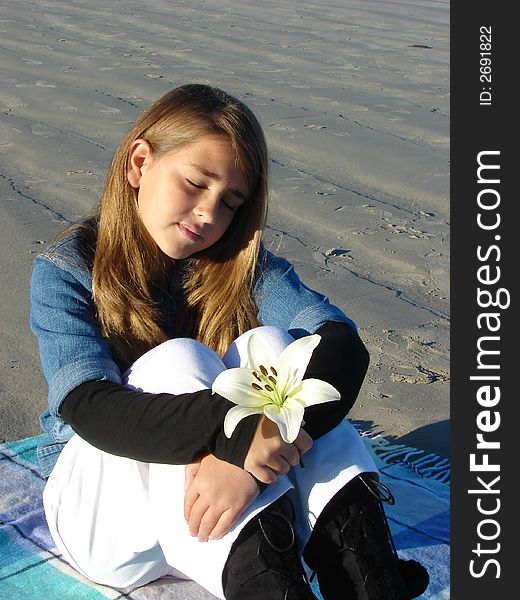 Young girl sitting on the beach with a flower in her hand, thinking of something. Young girl sitting on the beach with a flower in her hand, thinking of something